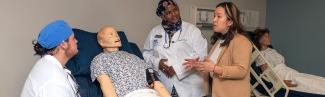 A group of students 从 different health programs discuss a diagnosis over a patient simulator